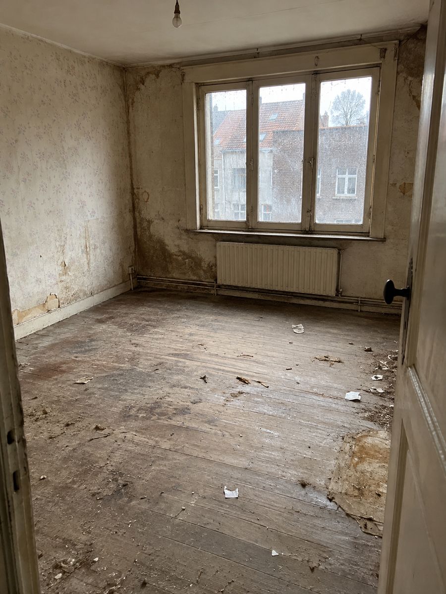 Pièce vide d’une maison ancienne, sol poussiéreux et taché, débris, toiles d’araignée et fenêtres sales