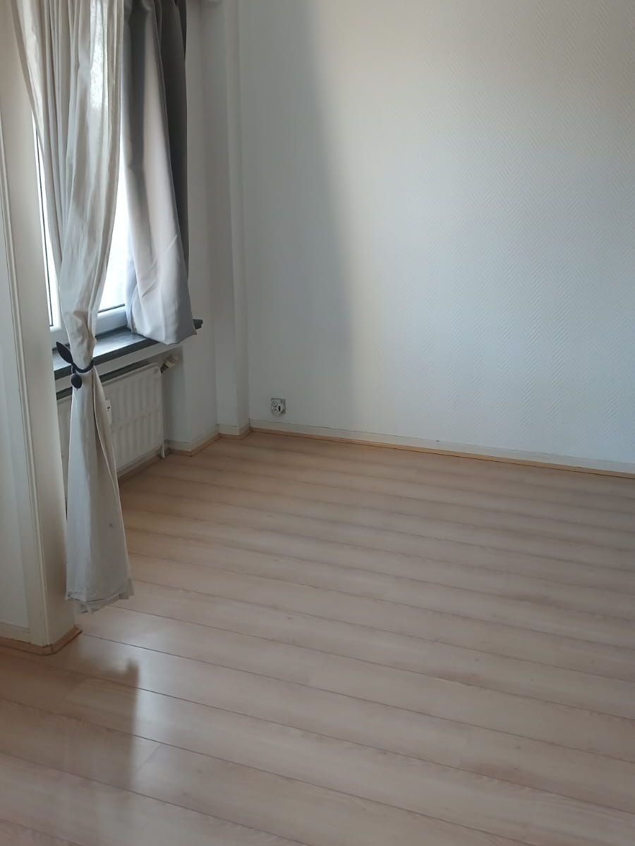 Chambre de l’appartement à Mons vidée et nettoyée, sol stratifié clair propre, rideaux et radiateur dégagés